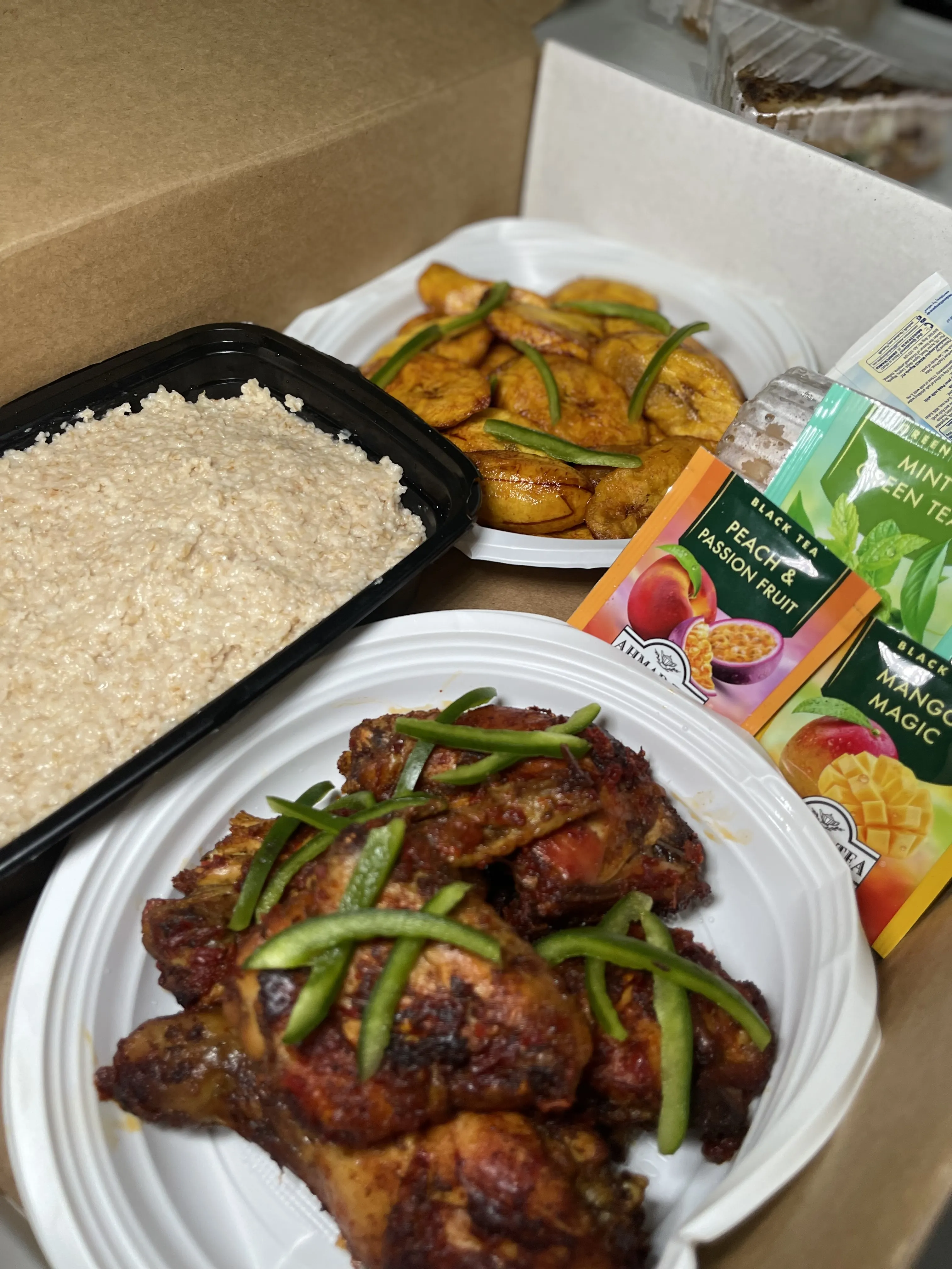 Breakfast box with coleslaw, fried plantain, peppered chicken, and assorted teas