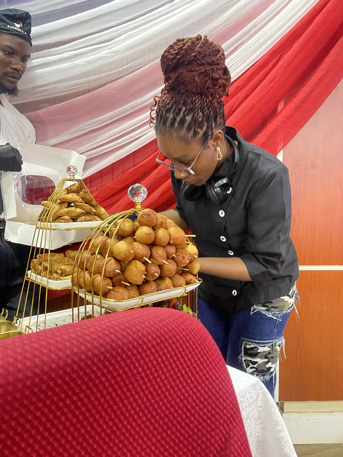 Server arranging puff puff and small chops on a tiered gold display stand at an event
