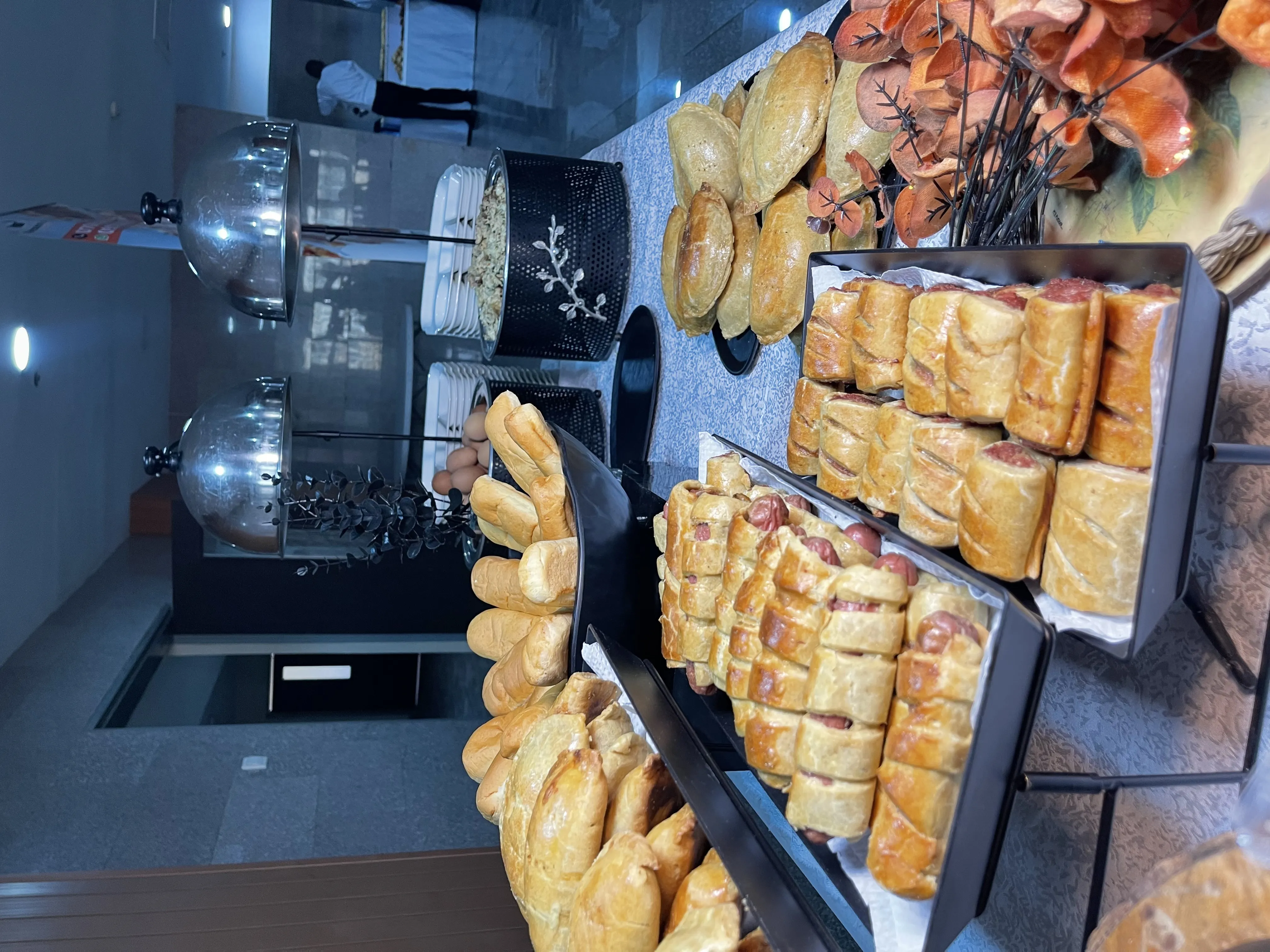 Tea break buffet setup with assorted bread rolls, sausage rolls, and meat pies